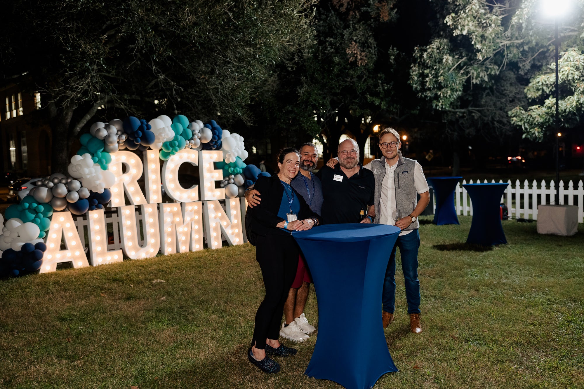 Rice alumni pose in front of a light up sign