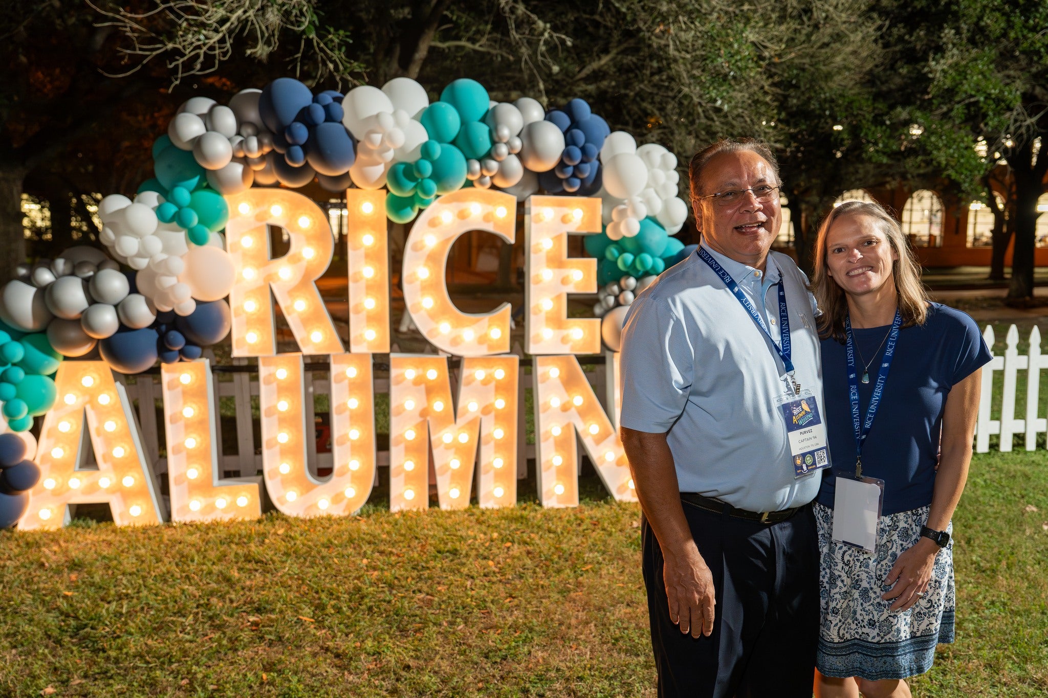 A man and a woman standing in front of a Rice Alumni light up sign